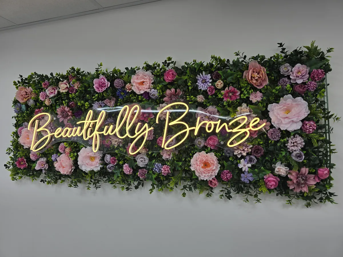 Beautifully Bronze’s illuminated name on the floral wall inside the salon